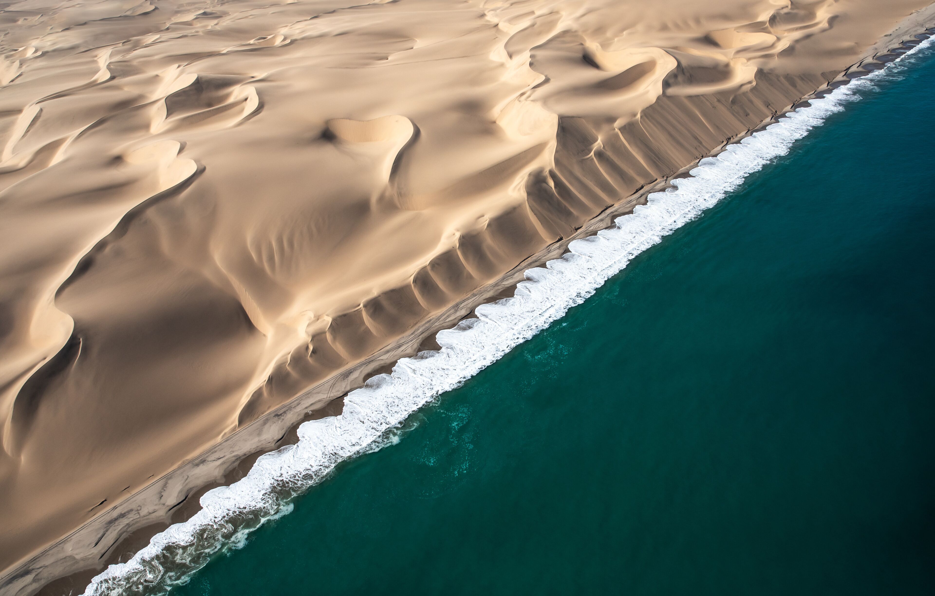 A vast desert landscape with sand dunes and a coastline.