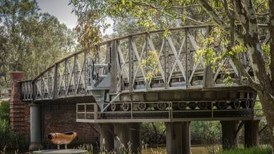 A steel bridge with a large wheel and a bird statue.