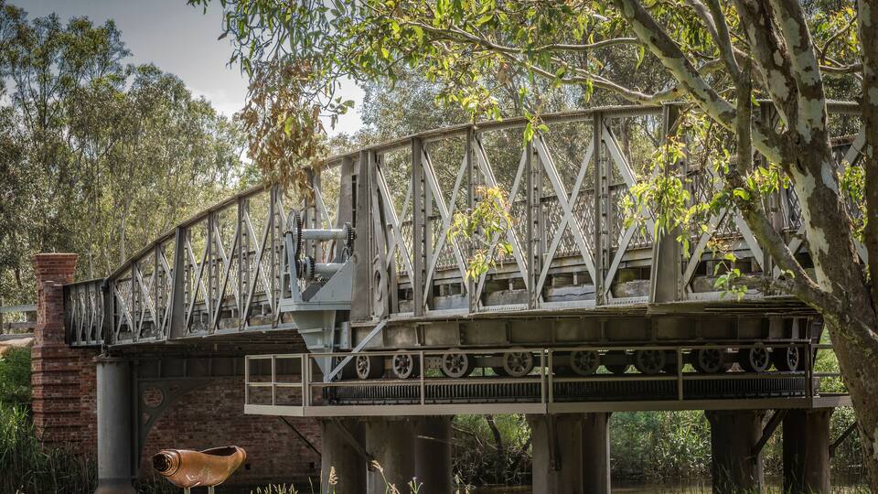 A steel bridge with a large wheel and a bird statue.