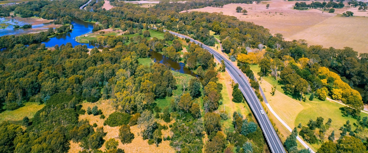 A winding highway through a forested area with a river and open fields.