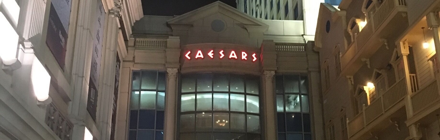 Vista noturna do hotel Caesars, com letreiros iluminados e edifícios ao redor.