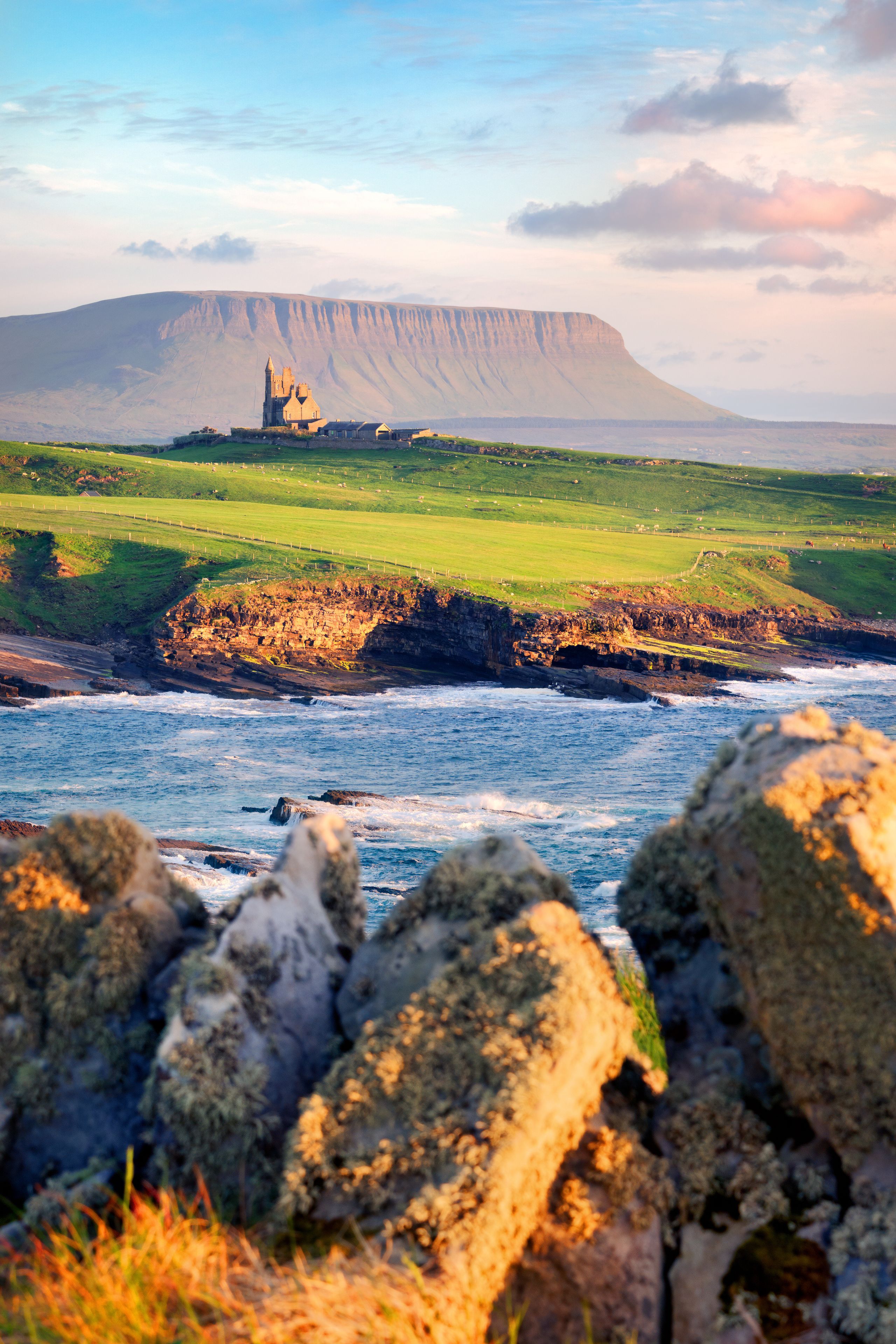 A coastal landscape with a prominent cliff, a castle, and a grassy field.
