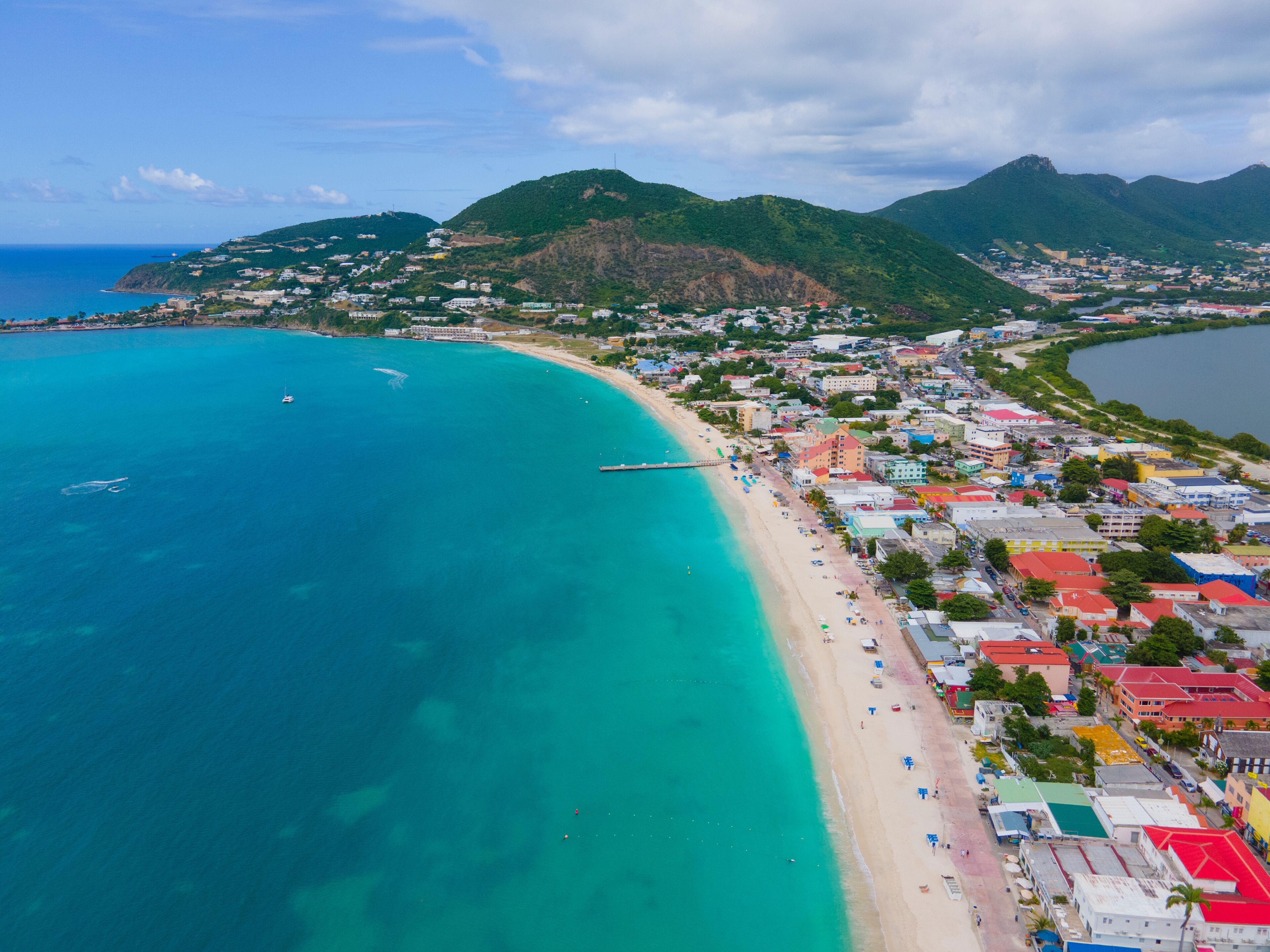 A coastal town with a beach, a pier, and mountains in the background.