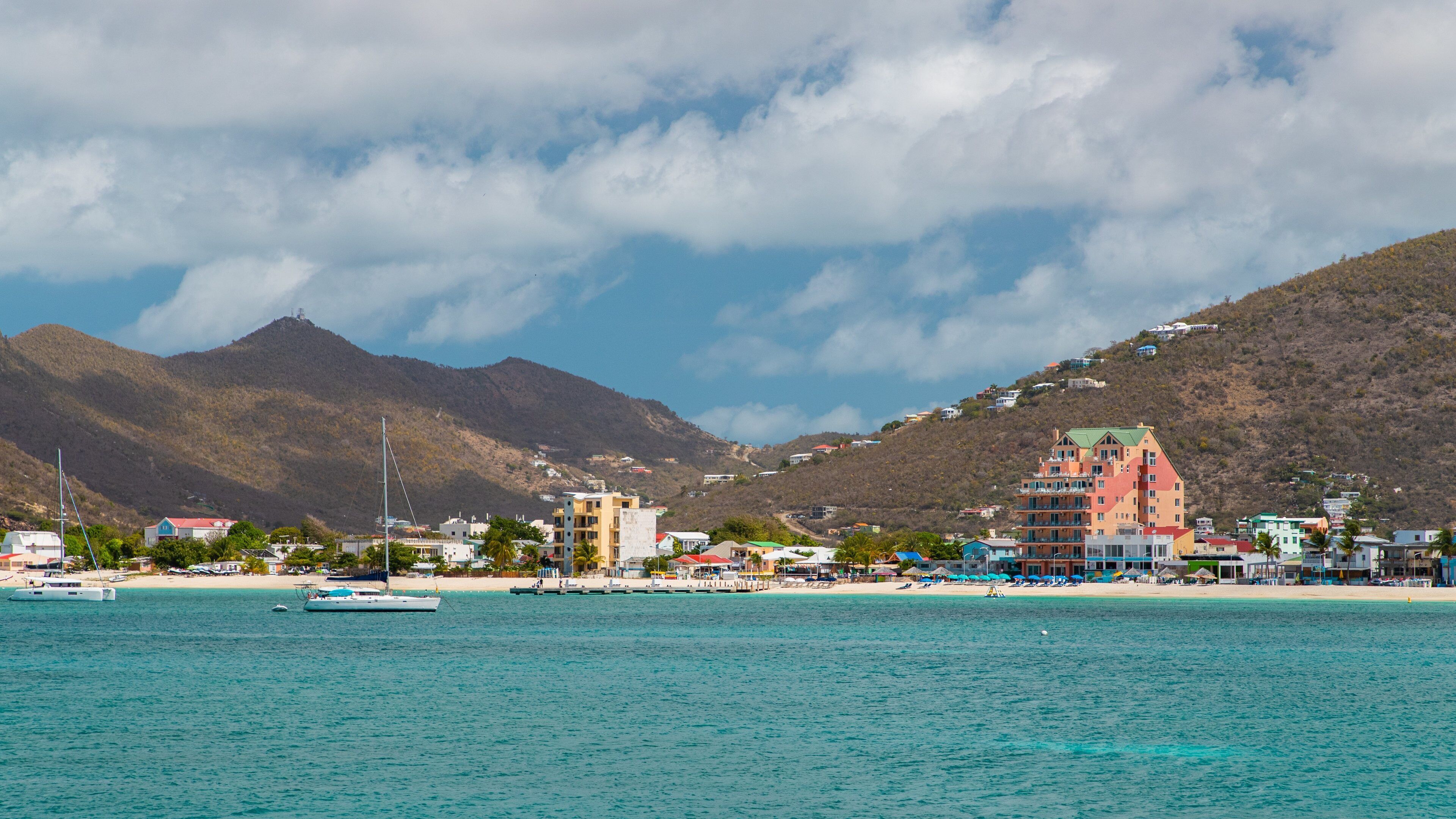 A coastal town with a beach, boats, and a mountain in the background.