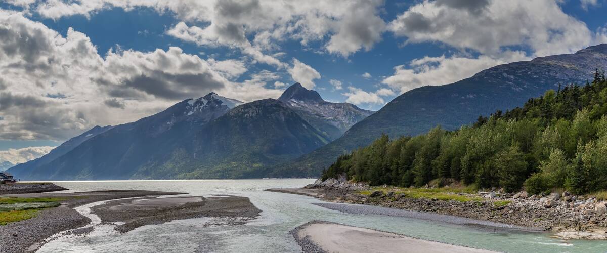 A river flowing through a mountainous landscape with a clear sky and a house on the left bank.