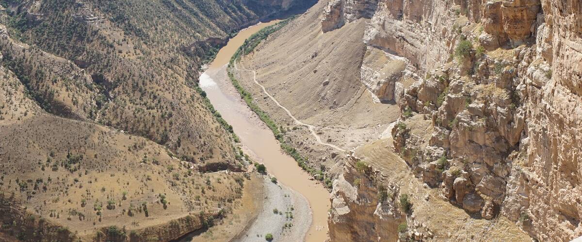 A canyon with a winding river, steep cliffs, and sparse vegetation.