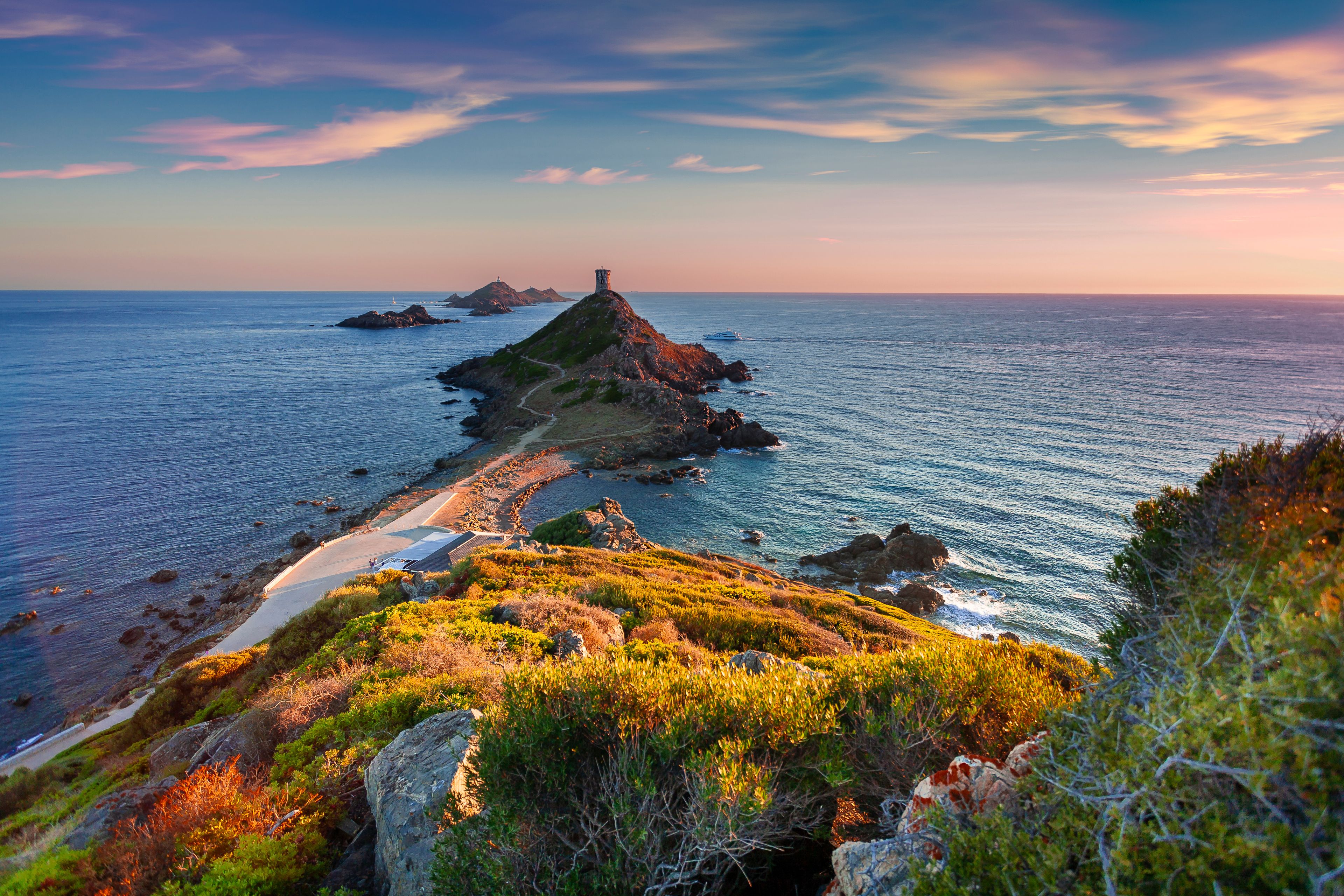 A coastal landscape with a lighthouse on a rocky outcrop, a clear sky, and calm sea.