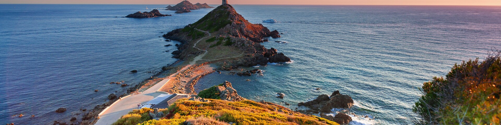 Un paisaje costero con un faro sobre un afloramiento rocoso, cielo despejado y mar en calma.