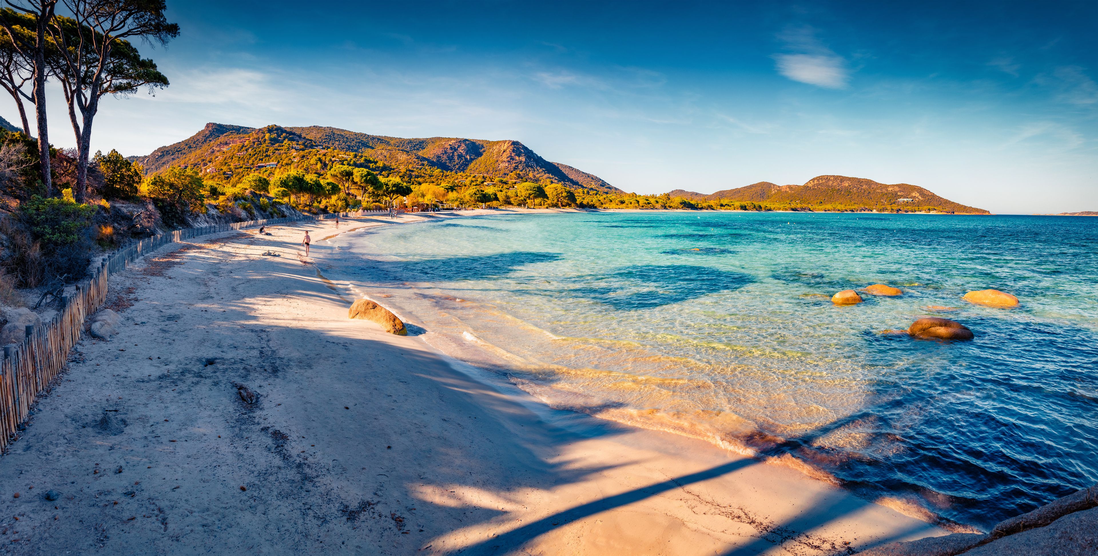 A beach with clear turquoise water, white sand, and rocky outcrops.