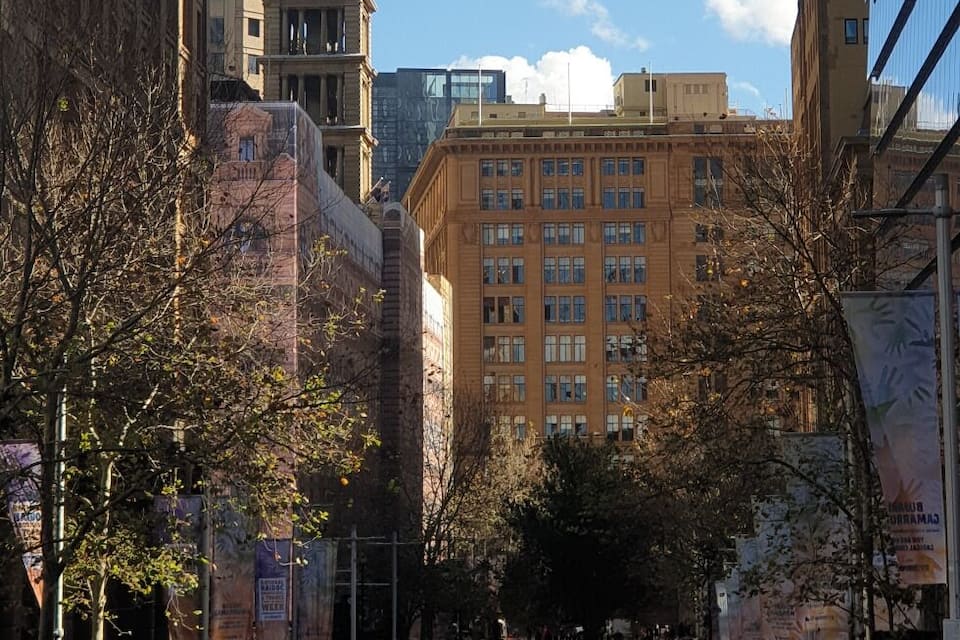 A city square with a historic clock tower, modern buildings, and pedestrians.