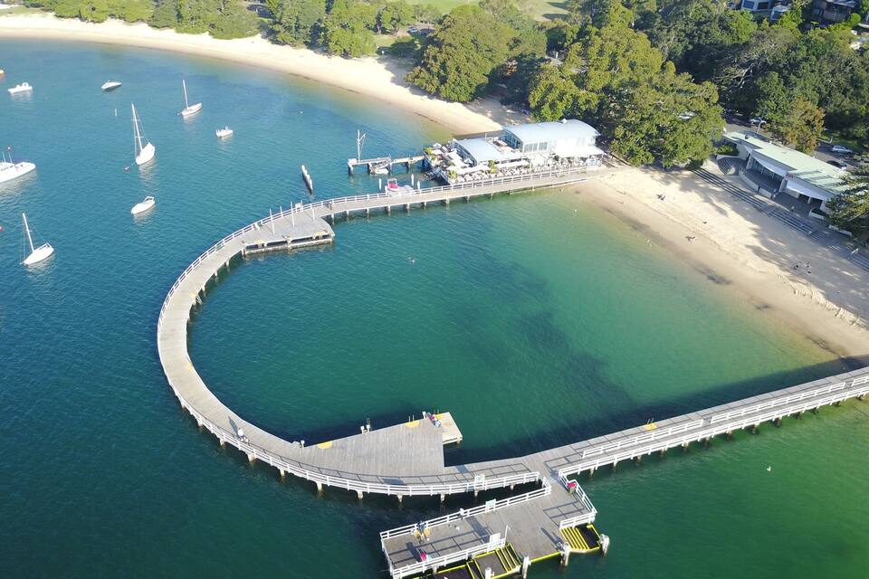 A coastal area with a curved pier extending into the water, surrounded by boats and a beach.