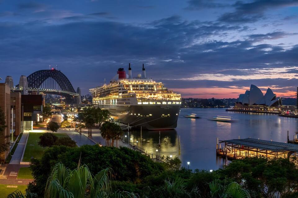 Un vaixell de creuer anomenat 'Queen Mary 2' amarrat prop de l'Opera de Sydney i el Pont de Sydney al capvespre.