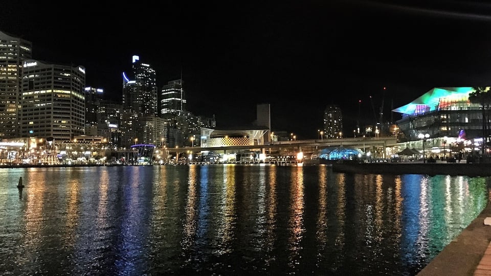 A nighttime cityscape with illuminated buildings reflecting on the water.