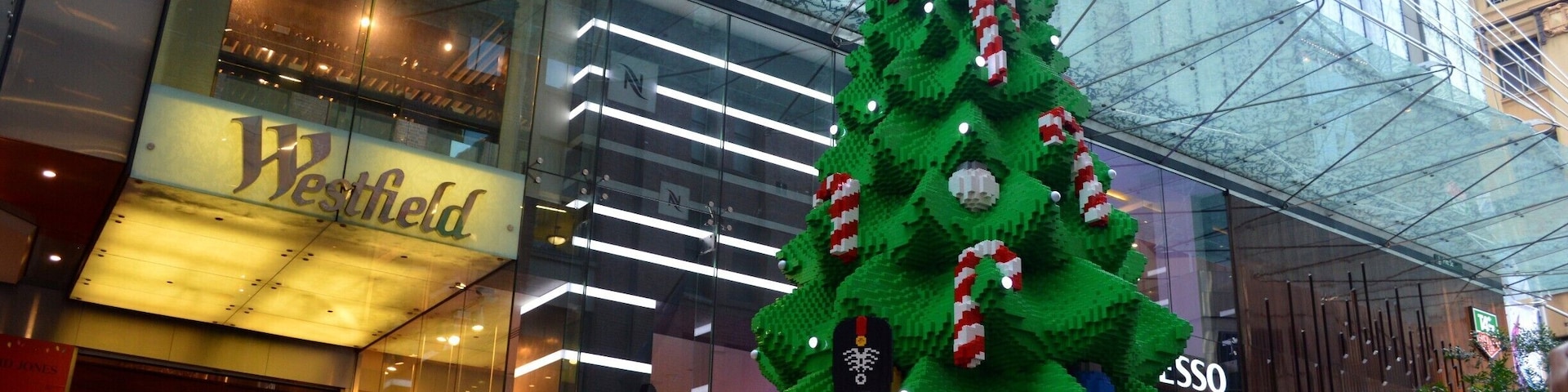 Un árbol de Navidad de LEGO con regalos frente a un centro comercial Westfield.