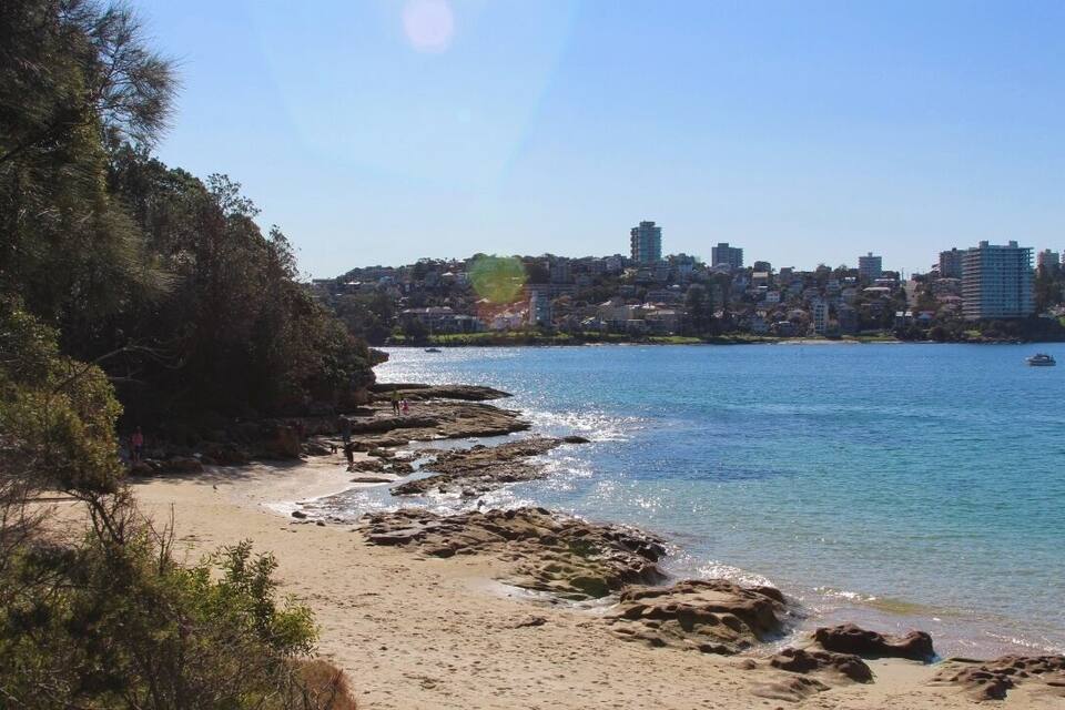 Paisatge costaner amb una platja sorrenca, línia de costa rocosa i edificis al fons.