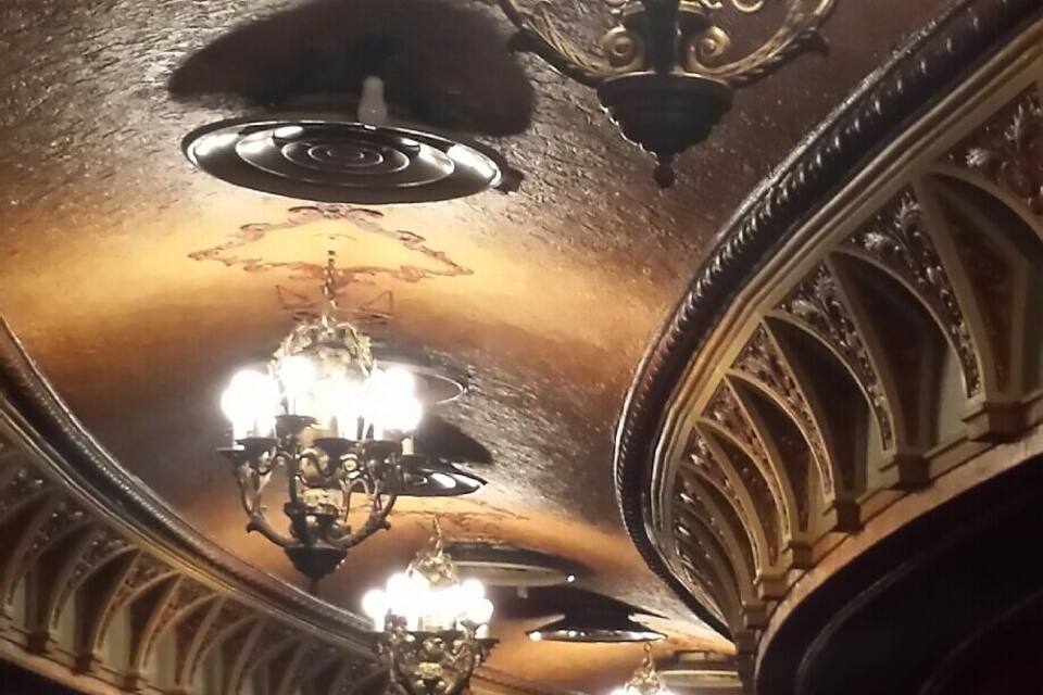 L'intérieur d'un théâtre somptueux, orné de nombreux lustres et rempli d'une foule de personnes.