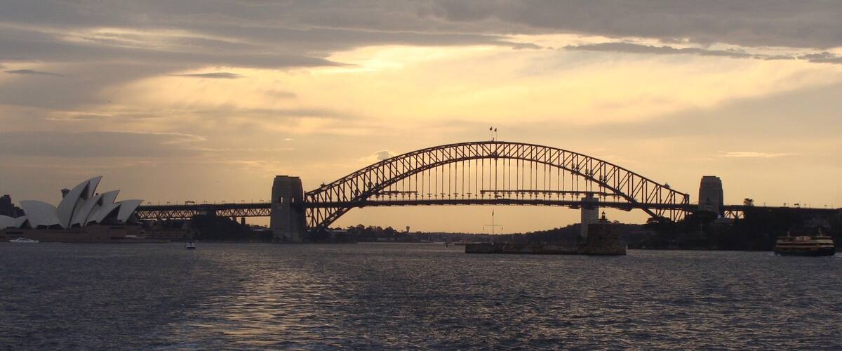 The Sydney Harbour Bridge with the Sydney Opera House in the background during sunset.