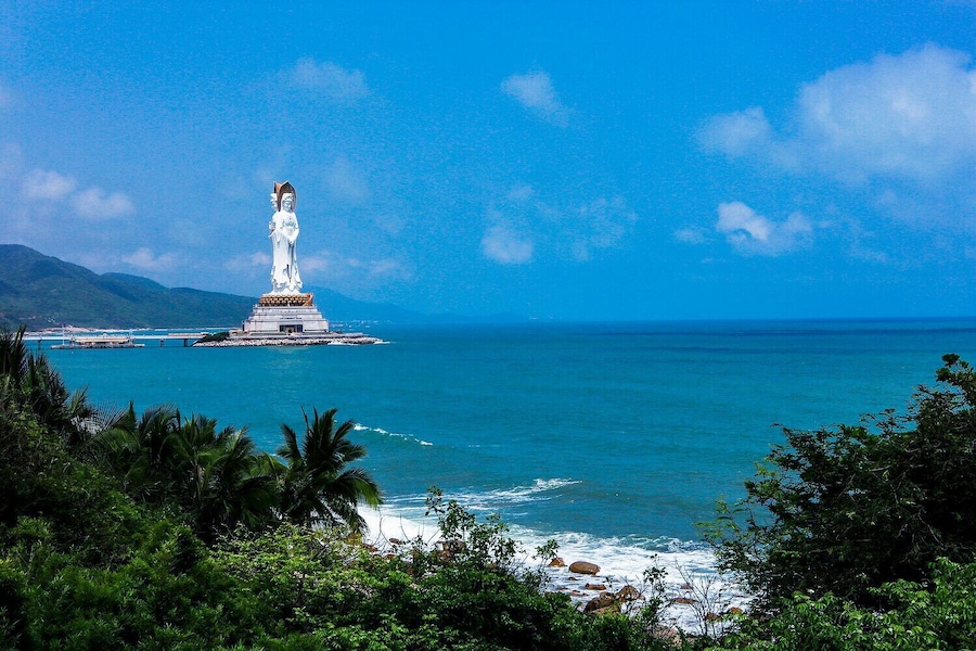 Una estatua en una pequeña isla rodeada de aguas turquesas y colinas verdes.