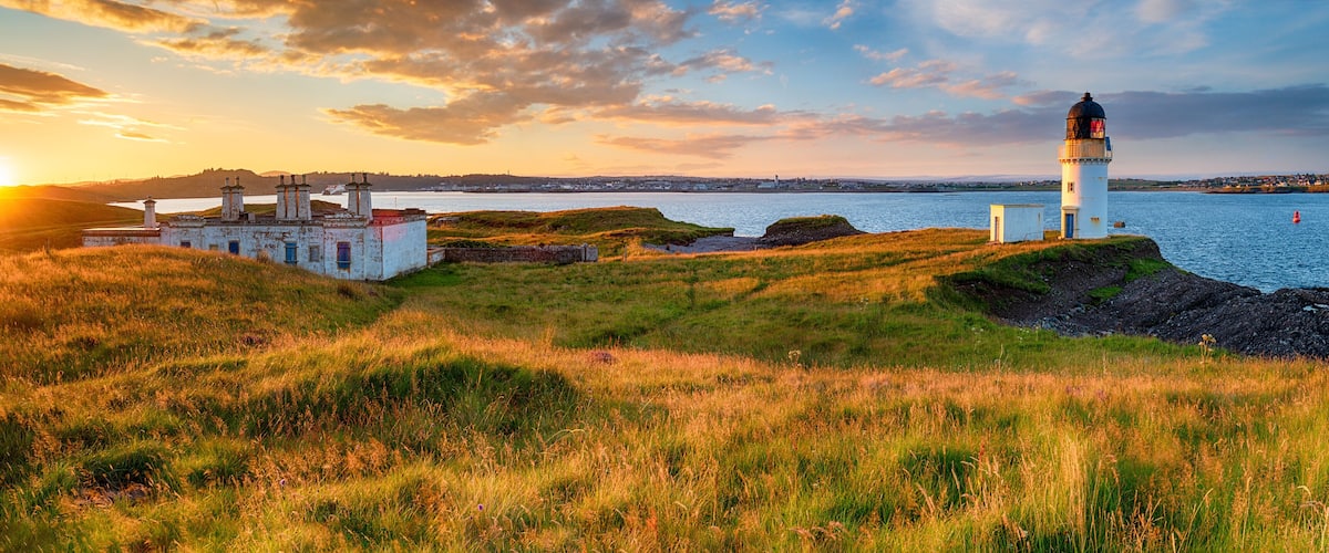 A lighthouse, grassy fields, and a sunset over water.