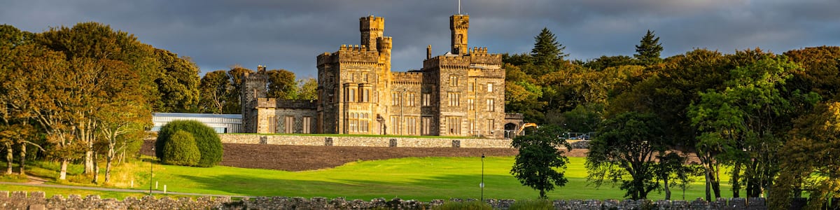 A historic castle by a lake with a well-maintained lawn and stone walls.
