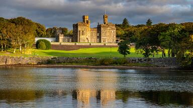 A historic castle by a lake with a well-maintained lawn and stone walls.