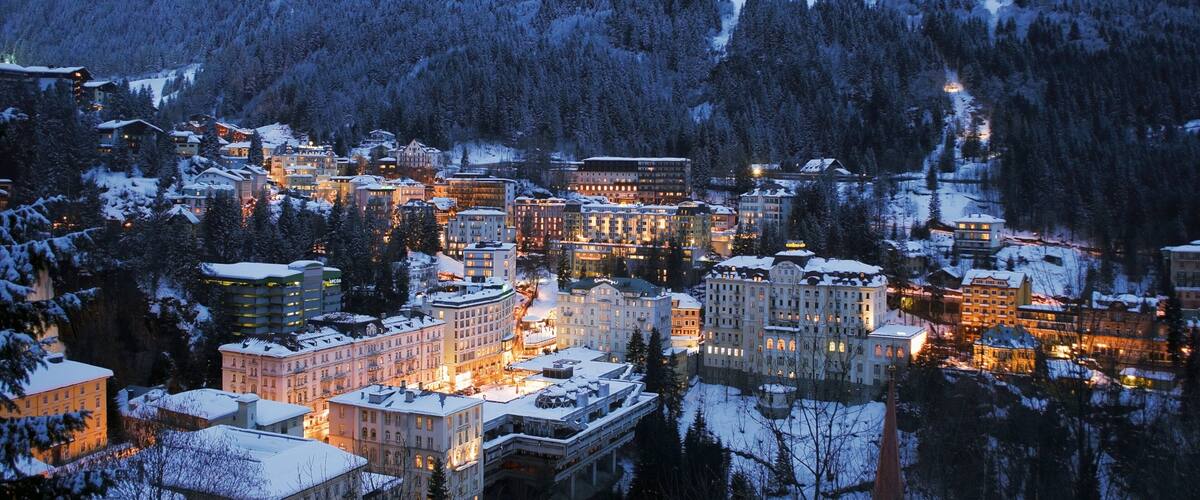 A snow-covered town with illuminated buildings and a mountain in the background.