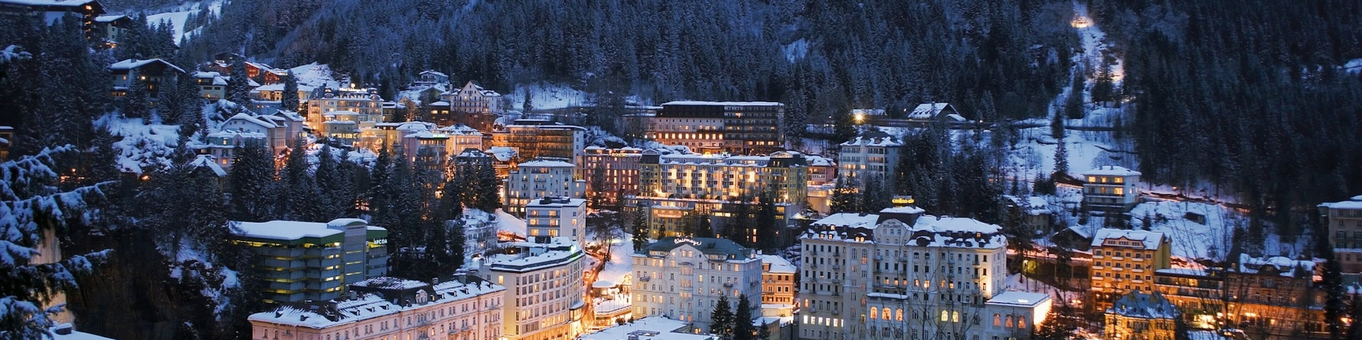 A snow-covered town with illuminated buildings and a mountain in the background.