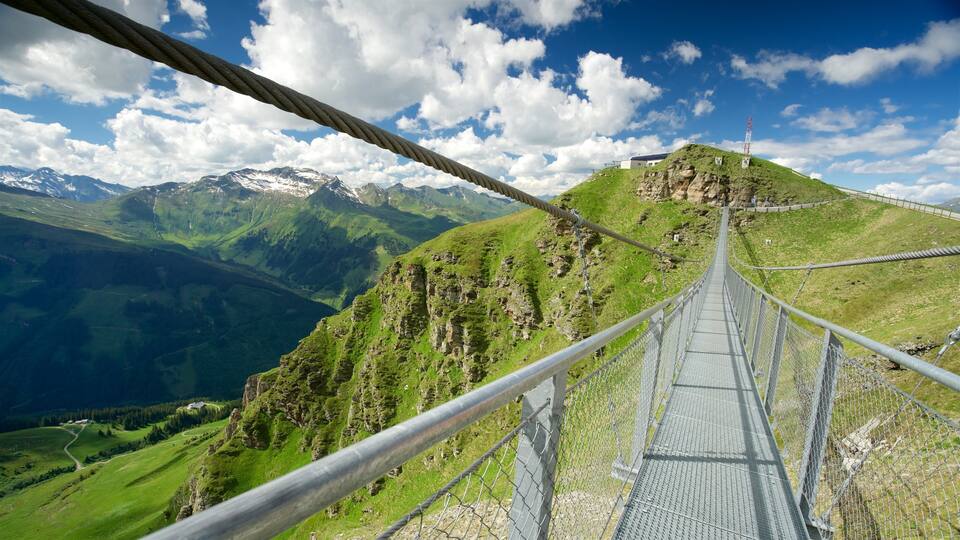 A suspension bridge with a view of green mountains and a clear blue sky.