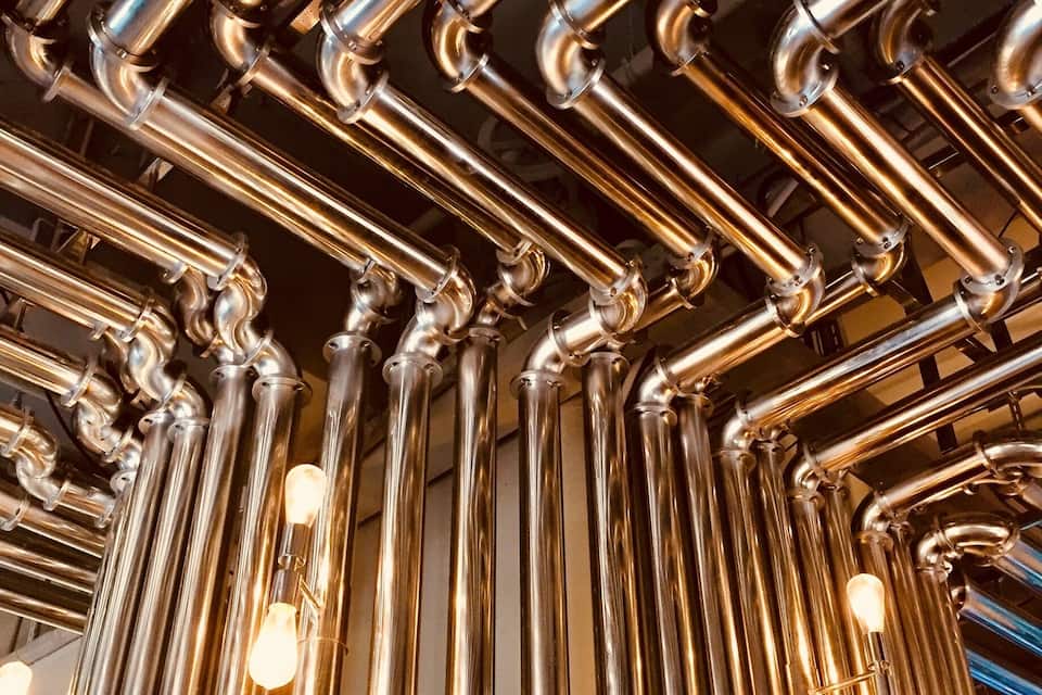A network of shiny, metallic pipes with light bulbs attached, likely part of an industrial or architectural structure.