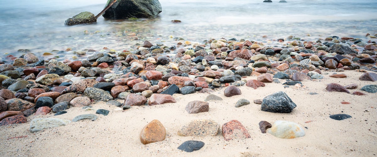 A pebbly beach with scattered rocks and calm water in the background.