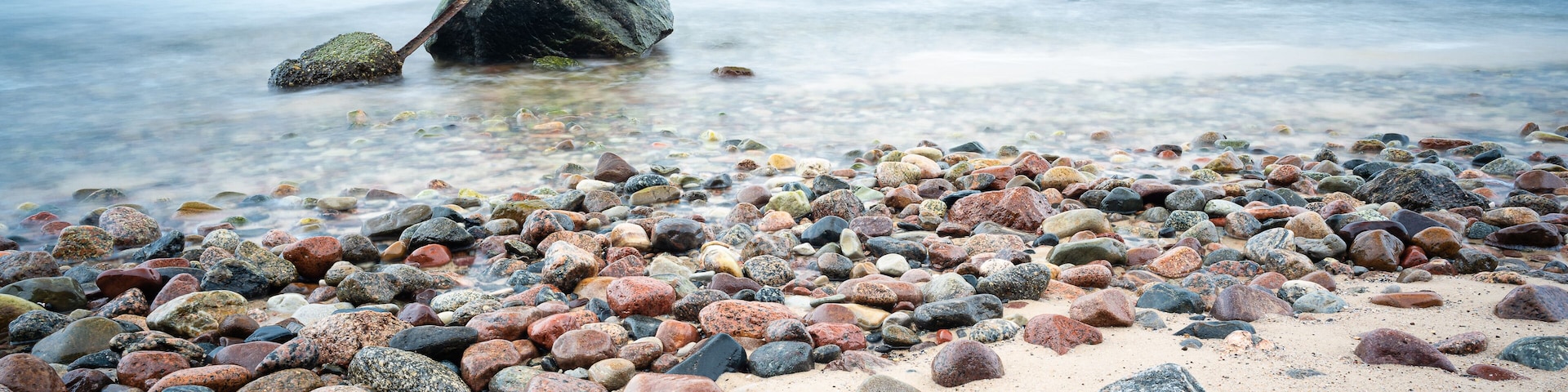 A pebbly beach with scattered rocks and calm water in the background.