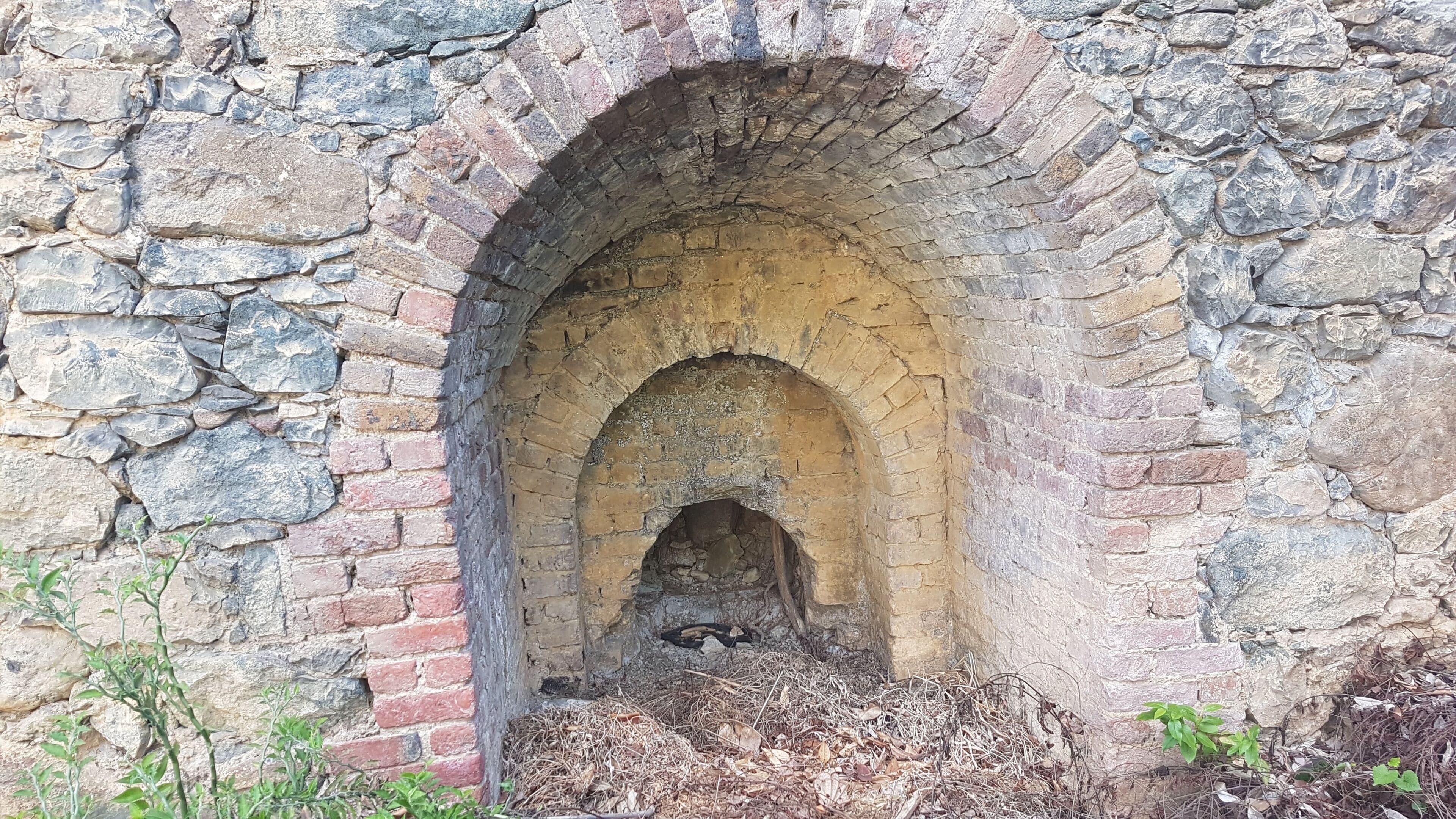 A stone archway with a brick base, surrounded by vegetation.