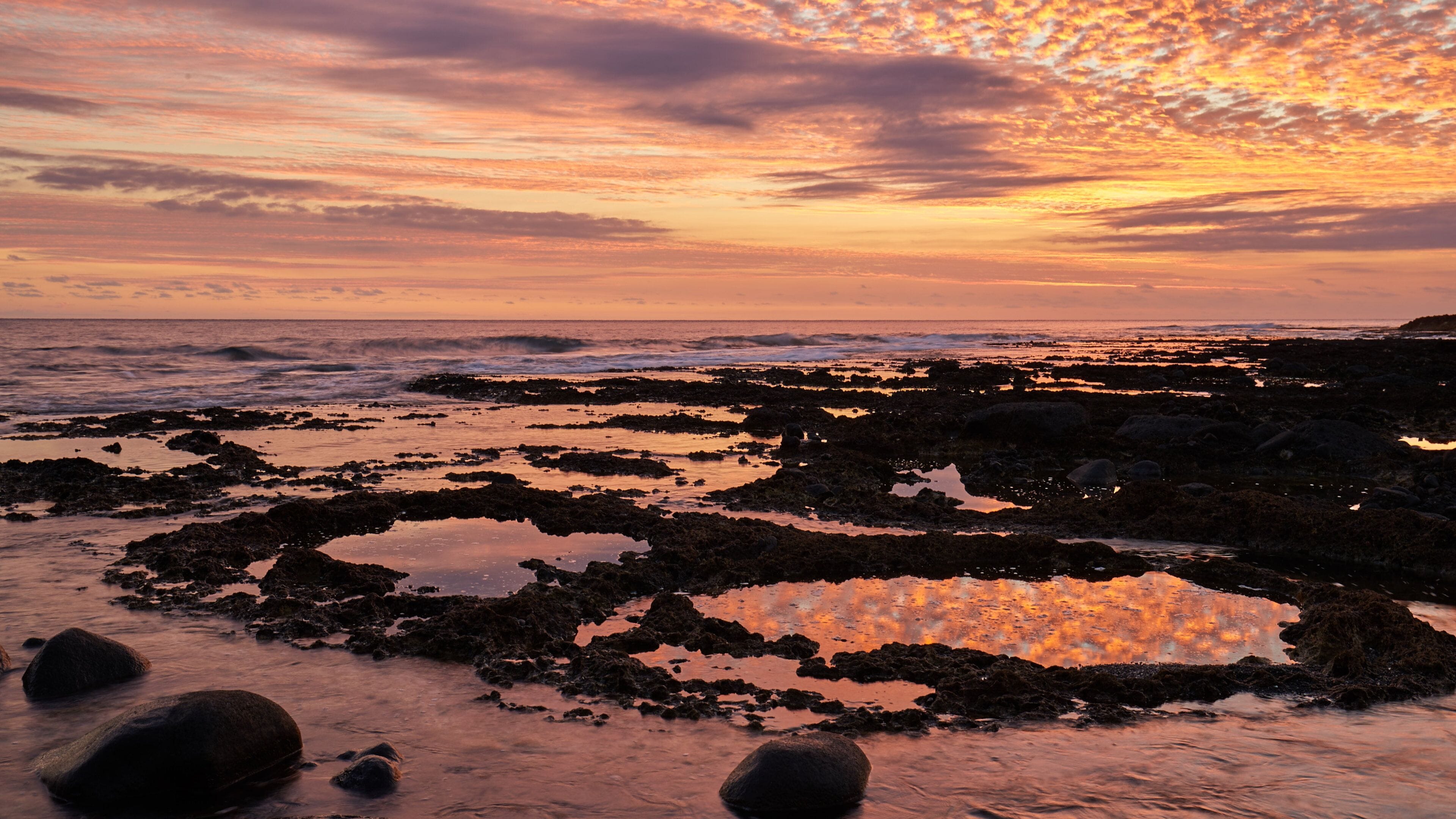 Linha costeira rochosa ao pôr do sol com um céu vibrante.