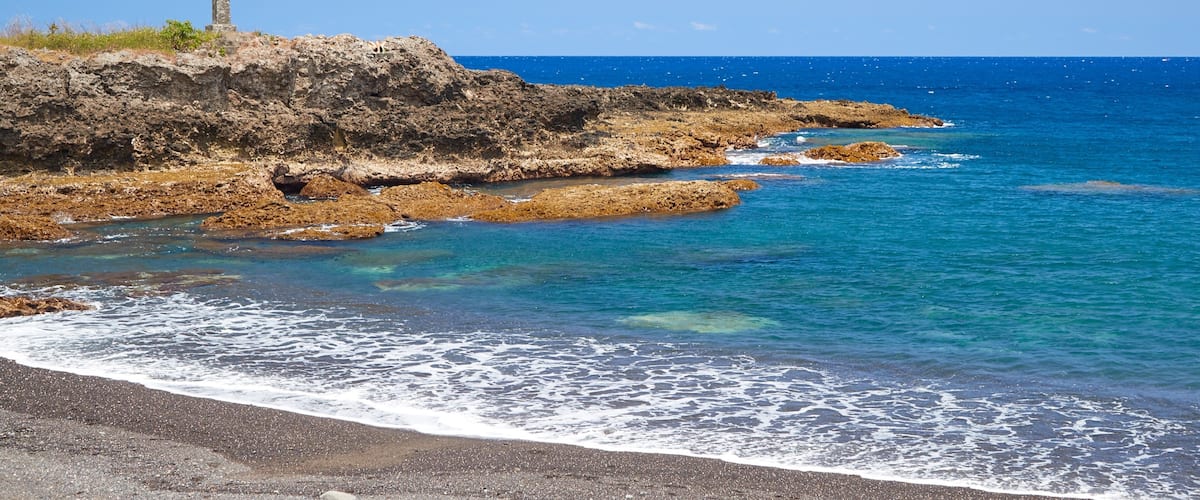 A rocky coastline with clear blue waters and a tall monument on a cliff.