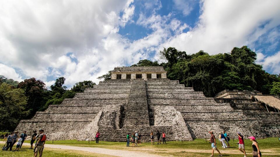 A large pyramid-like structure surrounded by lush greenery and a partly cloudy sky.