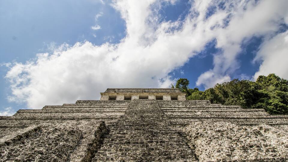 A large stone pyramid with a flat top, surrounded by dense green foliage.