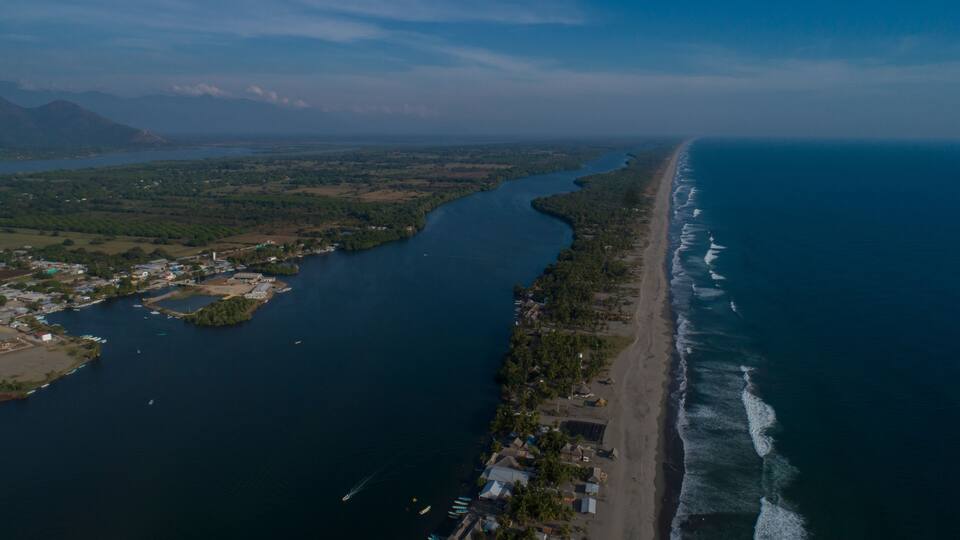 An aerial view of a coastal area with a long beach, a winding river, and scattered buildings along the shore.