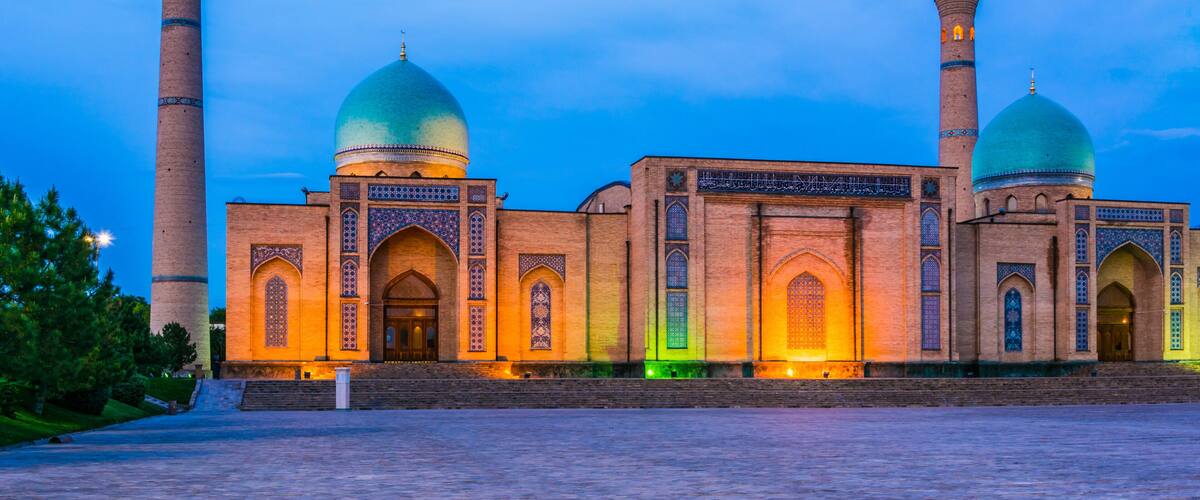 A mosque with two domes and two minarets, illuminated by warm lighting.
