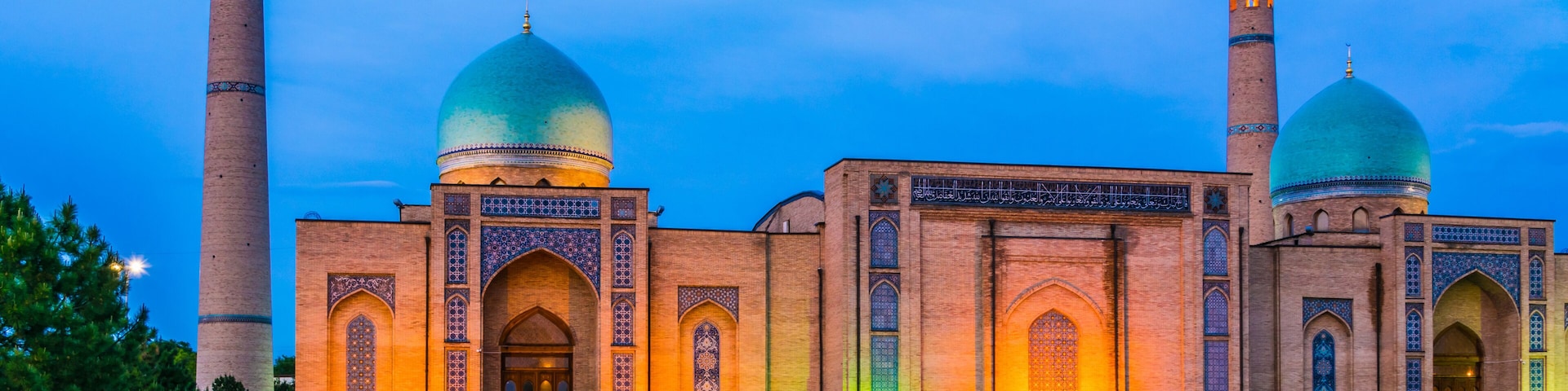 Una mezquita con dos cúpulas y dos minaretes, iluminada por una luz cálida.