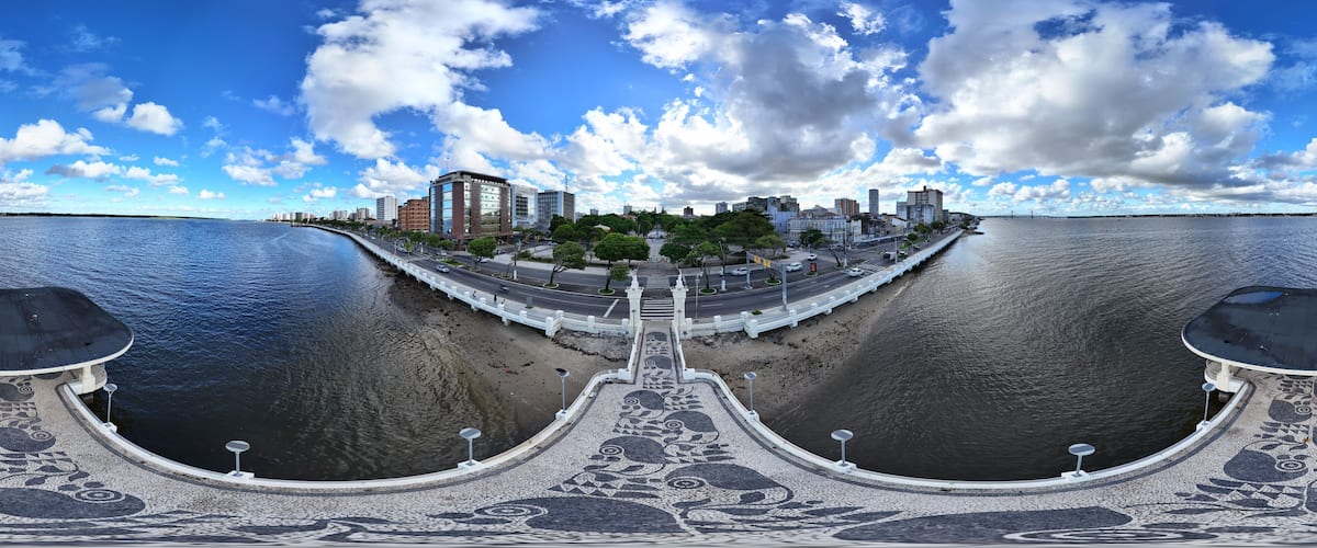 A waterfront cityscape with a bridge, buildings, and a patterned walkway.