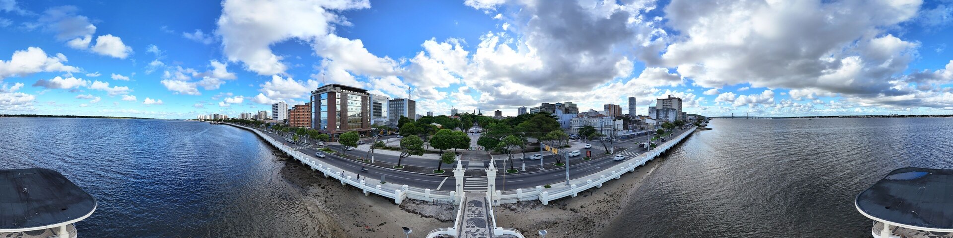 A waterfront cityscape with a bridge, buildings, and a patterned walkway.