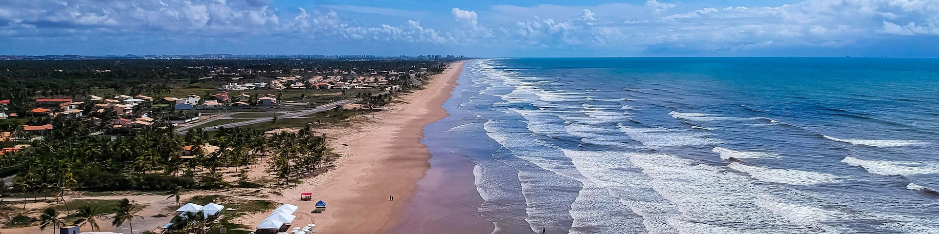 Uma praia costeira com uma extensa faixa de areia, ondas e uma fileira de guarda-sóis.