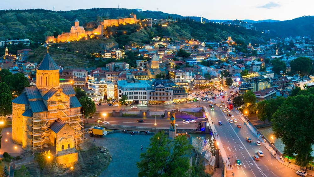 The evening panorama of the old town in the old district of Avlabari, Holy Trinity Cathedral and Rike Park, the Kura river reflects the evening city lights in Tbilisi, Georgia.
