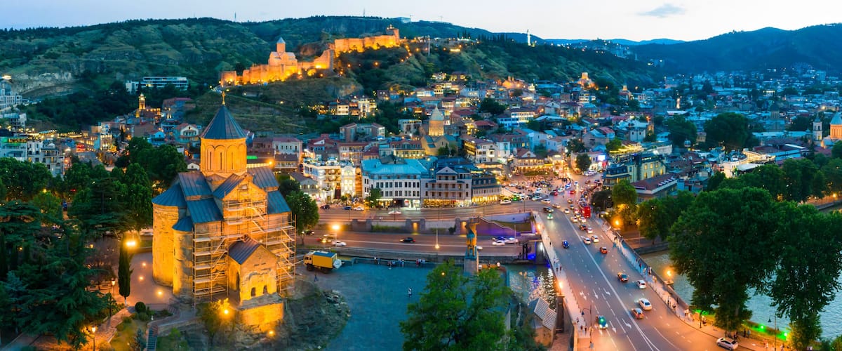 The evening panorama of the old town in the old district of Avlabari, Holy Trinity Cathedral and Rike Park, the Kura river reflects the evening city lights in Tbilisi, Georgia.