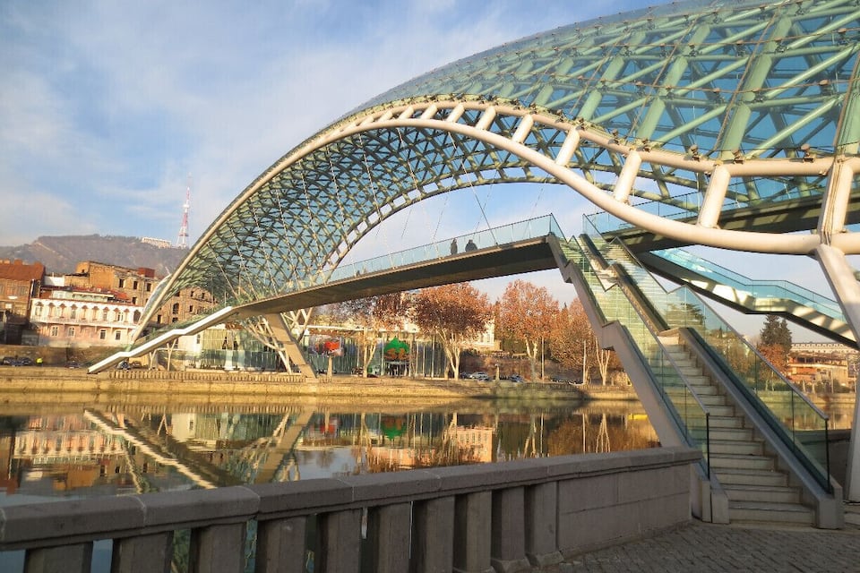 Un pont de vidre modern sobre un riu, amb un paisatge urbà al fons.