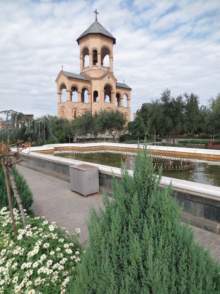 A historic church with a bell tower, surrounded by a water feature and greenery.