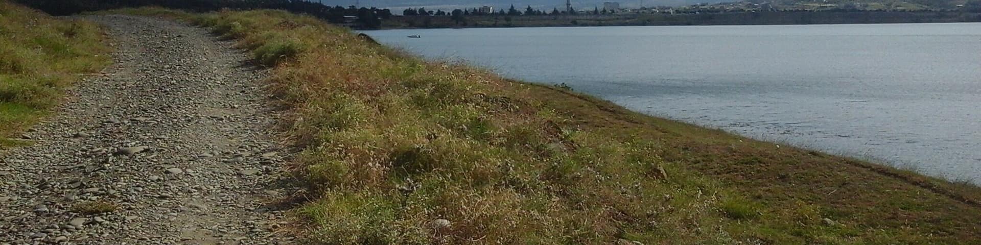 A gravel path beside a lake with mountains in the background.