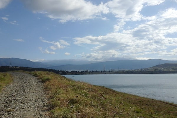 Un sentier de gravier longe un lac, avec des montagnes en arrière-plan.