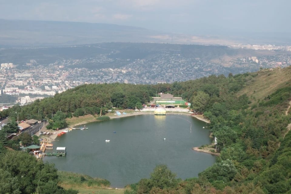 Un lago rodeado de colinas con una ciudad al fondo.