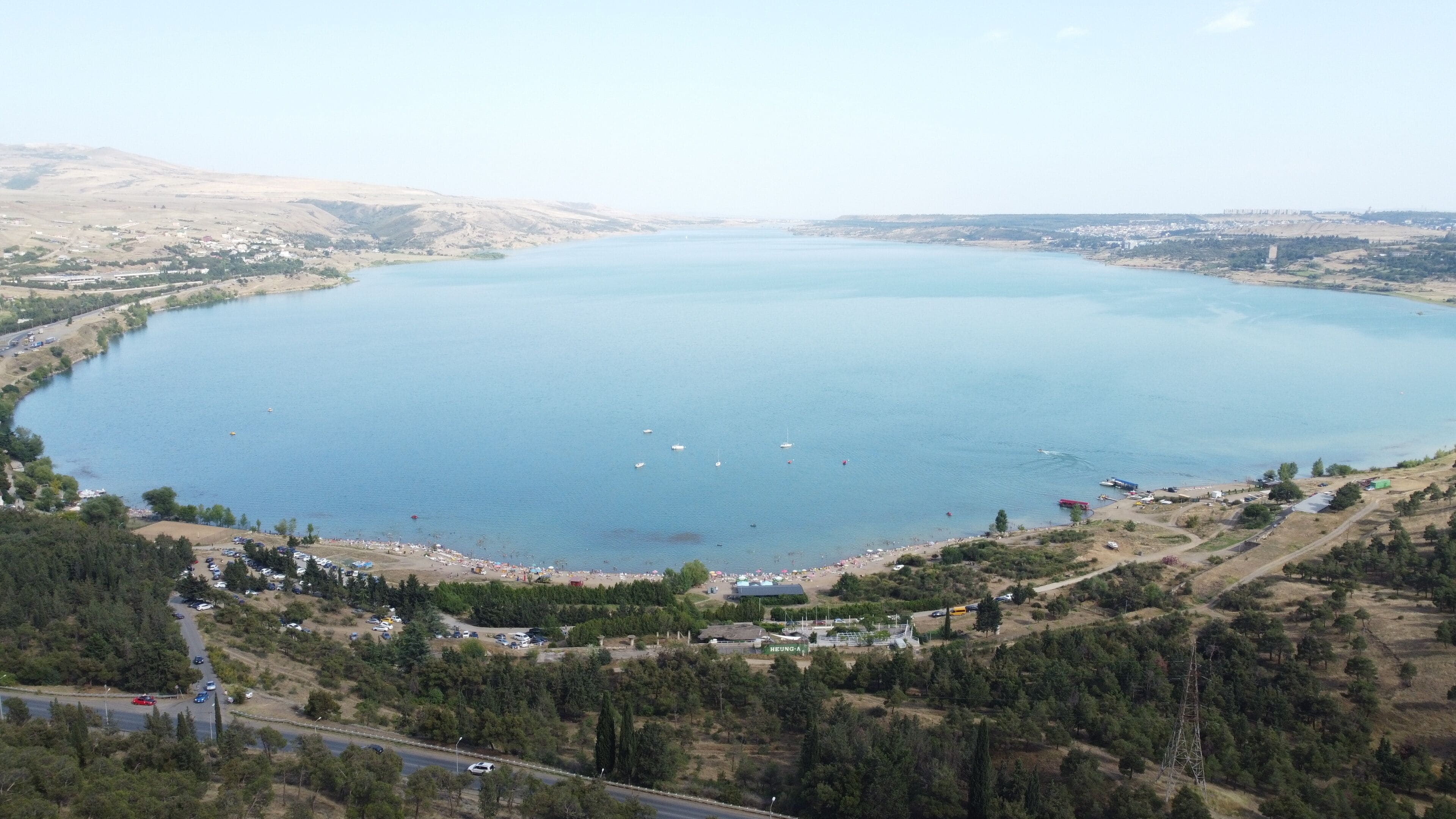 A large lake surrounded by hills and a small town with visible buildings and parked cars.